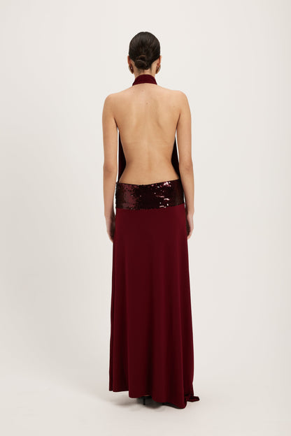XL - Women's dark red maxi dress featuring a draped cowl halter neckline, an open back, and a wide sequin-embellished band at the waist, falling to a floor-length hem.