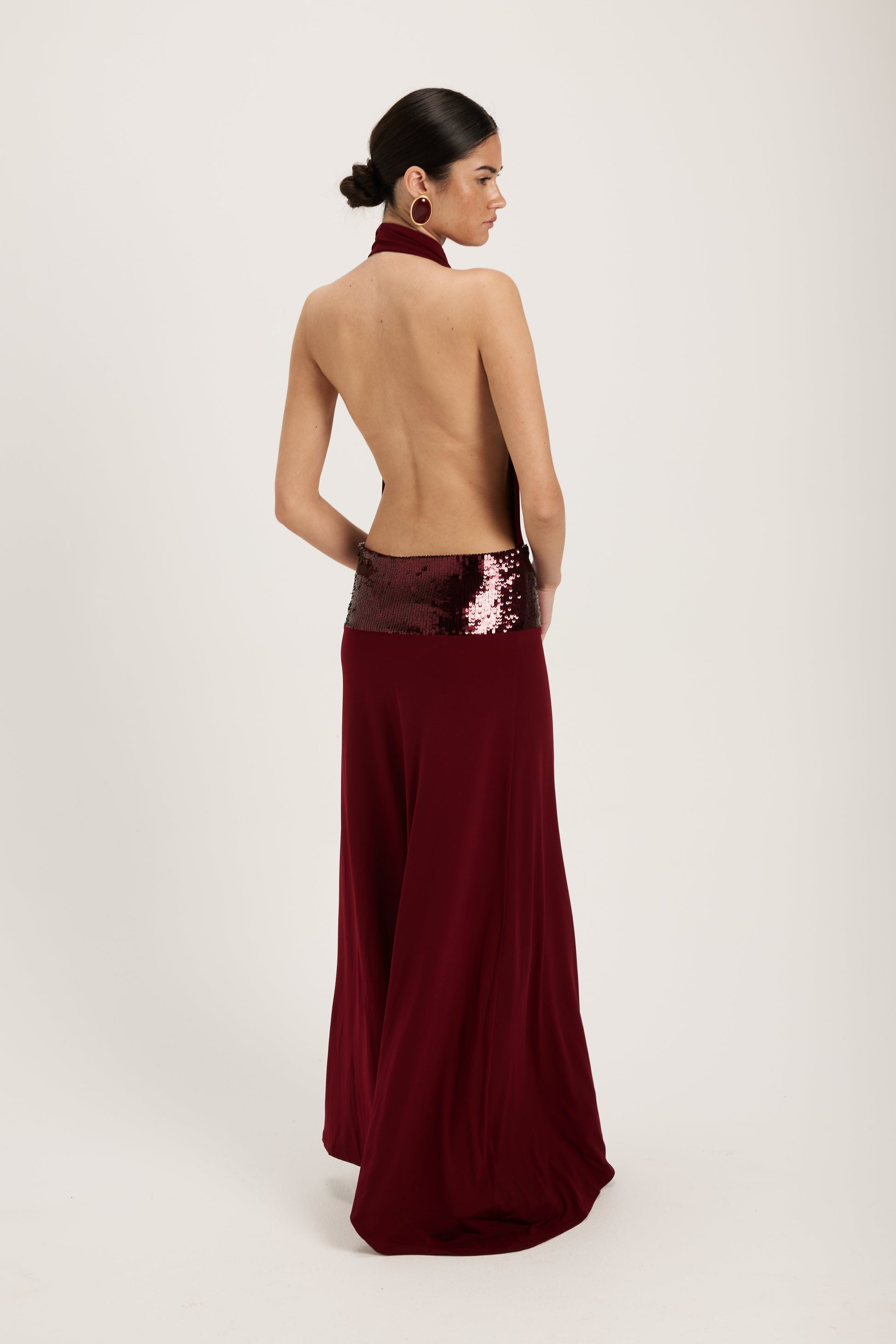 XL - Women's dark red maxi dress featuring a draped cowl halter neckline, an open back, and a wide sequin-embellished band at the waist, falling to a floor-length hem.