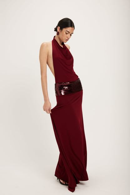 XL - Women's dark red maxi dress featuring a draped cowl halter neckline, an open back, and a wide sequin-embellished band at the waist, falling to a floor-length hem.