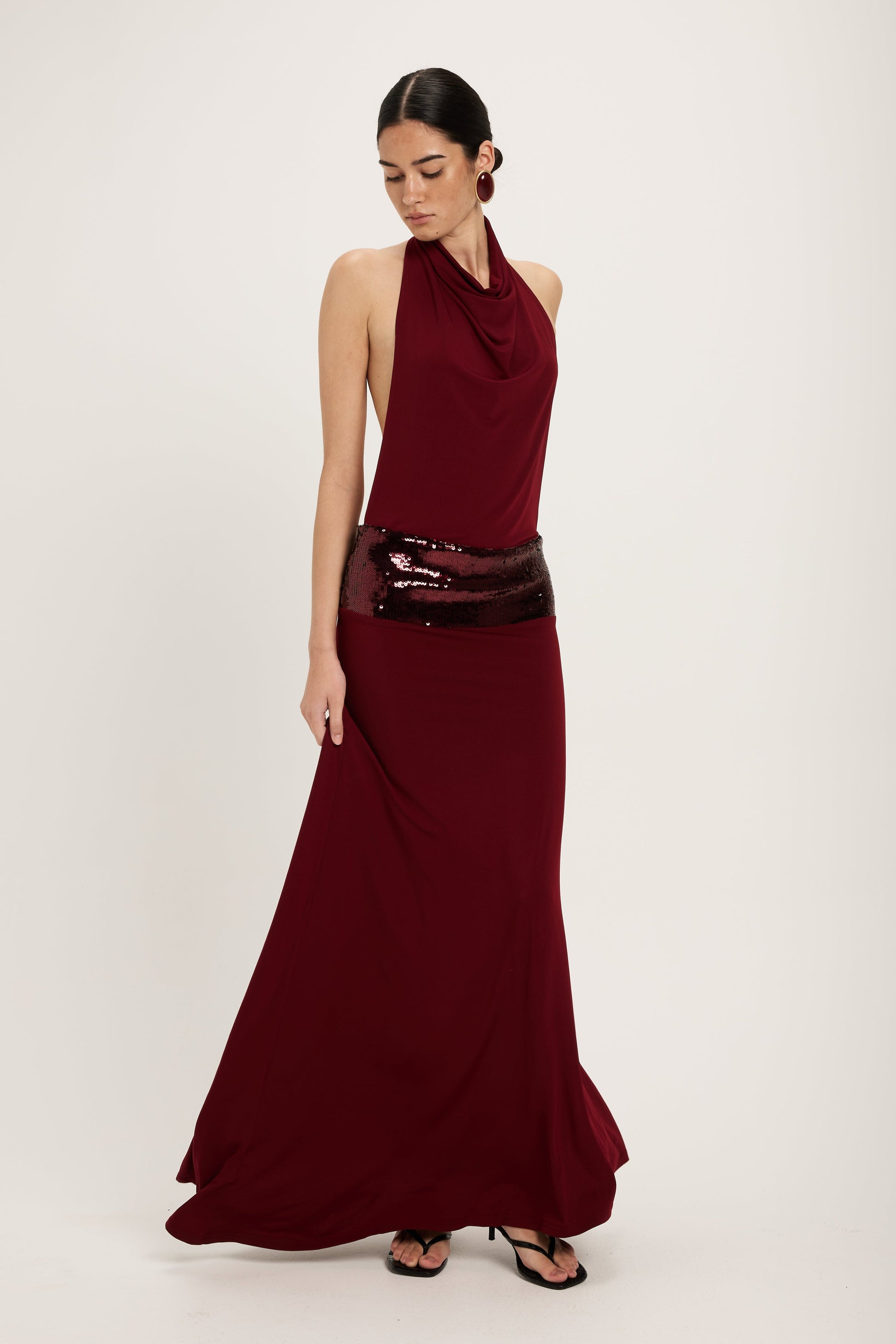 XL - Women's dark red maxi dress featuring a draped cowl halter neckline, an open back, and a wide sequin-embellished band at the waist, falling to a floor-length hem.