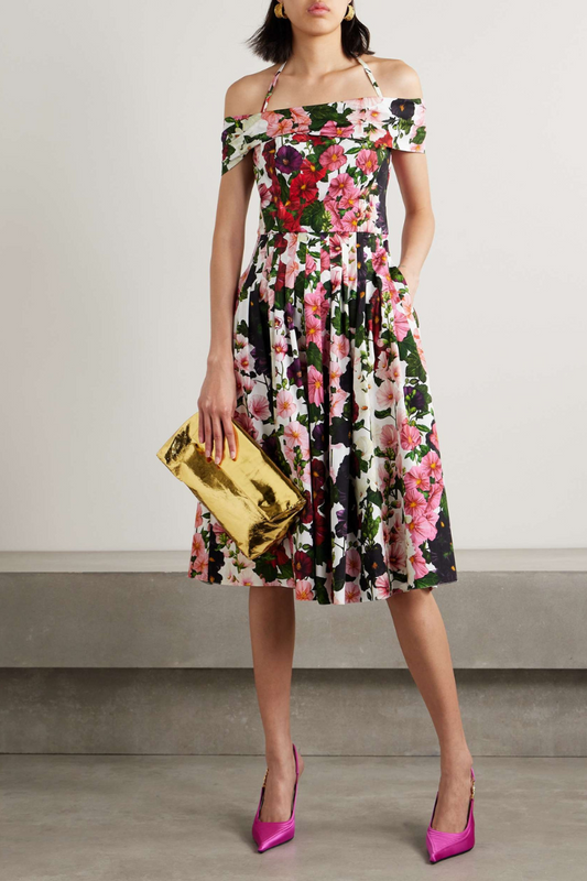 Multicolor - A woman models an off-the-shoulder halter midi dress with a vibrant, large-scale floral print in shades of pink, red, and purple on a white background. The dress has a fitted bodice, a pleated A-line skirt, and she has one hand in a side pocket. She is holding a metallic gold clutch and wearing fuchsia pointed-toe heels.