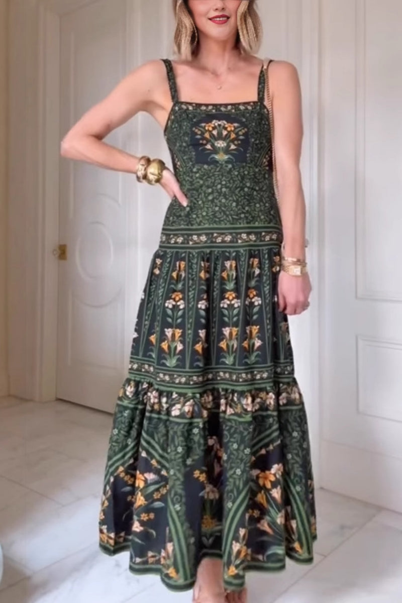 Green - Woman wearing a dark green and black maxi dress featuring a square neckline, wide straps, a tiered skirt, and an intricate botanical floral border print.