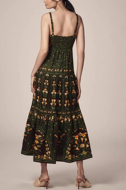 Green - Woman wearing a dark green and black maxi dress featuring a square neckline, wide straps, a tiered skirt, and an intricate botanical floral border print.