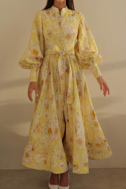 Yellow - A woman wearing a yellow maxi dress with a large white floral print, featuring long balloon sleeves, a button-down front, and a tie waist.