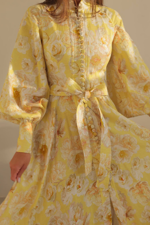 Yellow - A woman wearing a yellow maxi dress with a large white floral print, featuring long balloon sleeves, a button-down front, and a tie waist.
