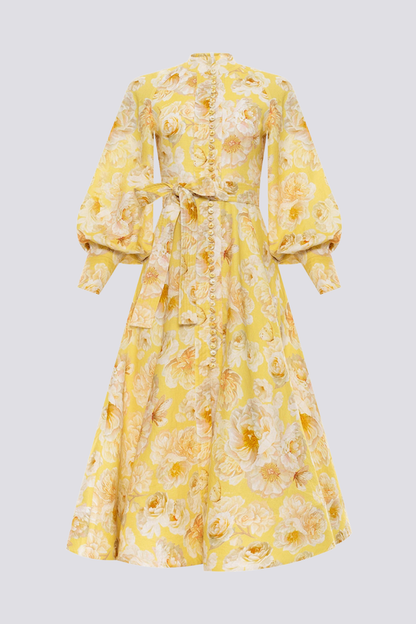 Yellow - A woman wearing a yellow maxi dress with a large white floral print, featuring long balloon sleeves, a button-down front, and a tie waist.