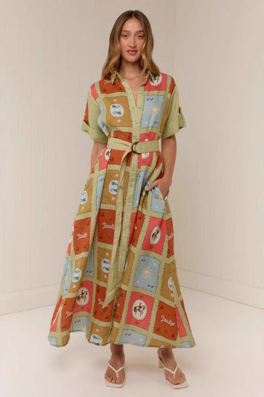 Multicolored - A woman wearing a long, short-sleeved shirt dress featuring a colourful patchwork tile print with whimsical motifs. The dress has a button-down front, a collar, a matching waist belt, and side pockets.