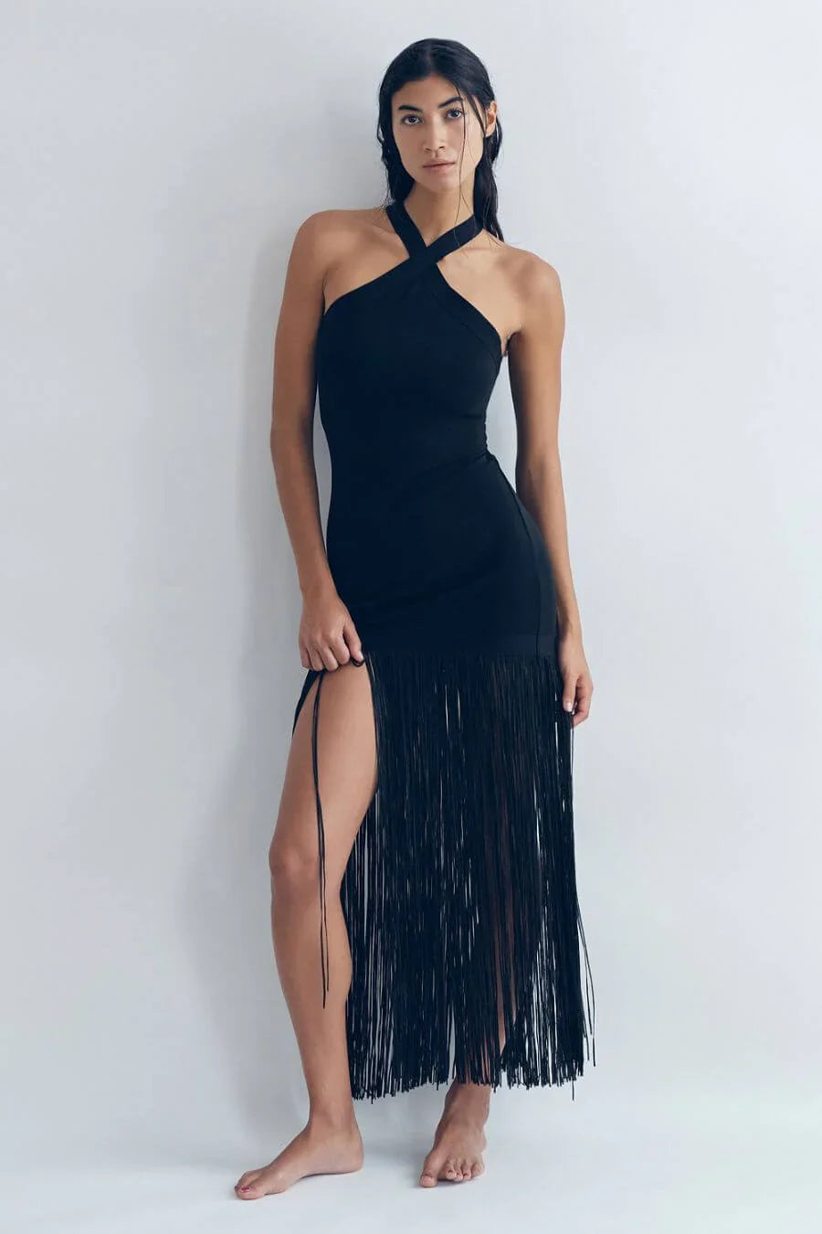 Woman wearing an elegant black evening dress featuring a fitted crossover halter bodice and a dramatic floor-length fringe skirt with a high side slit.