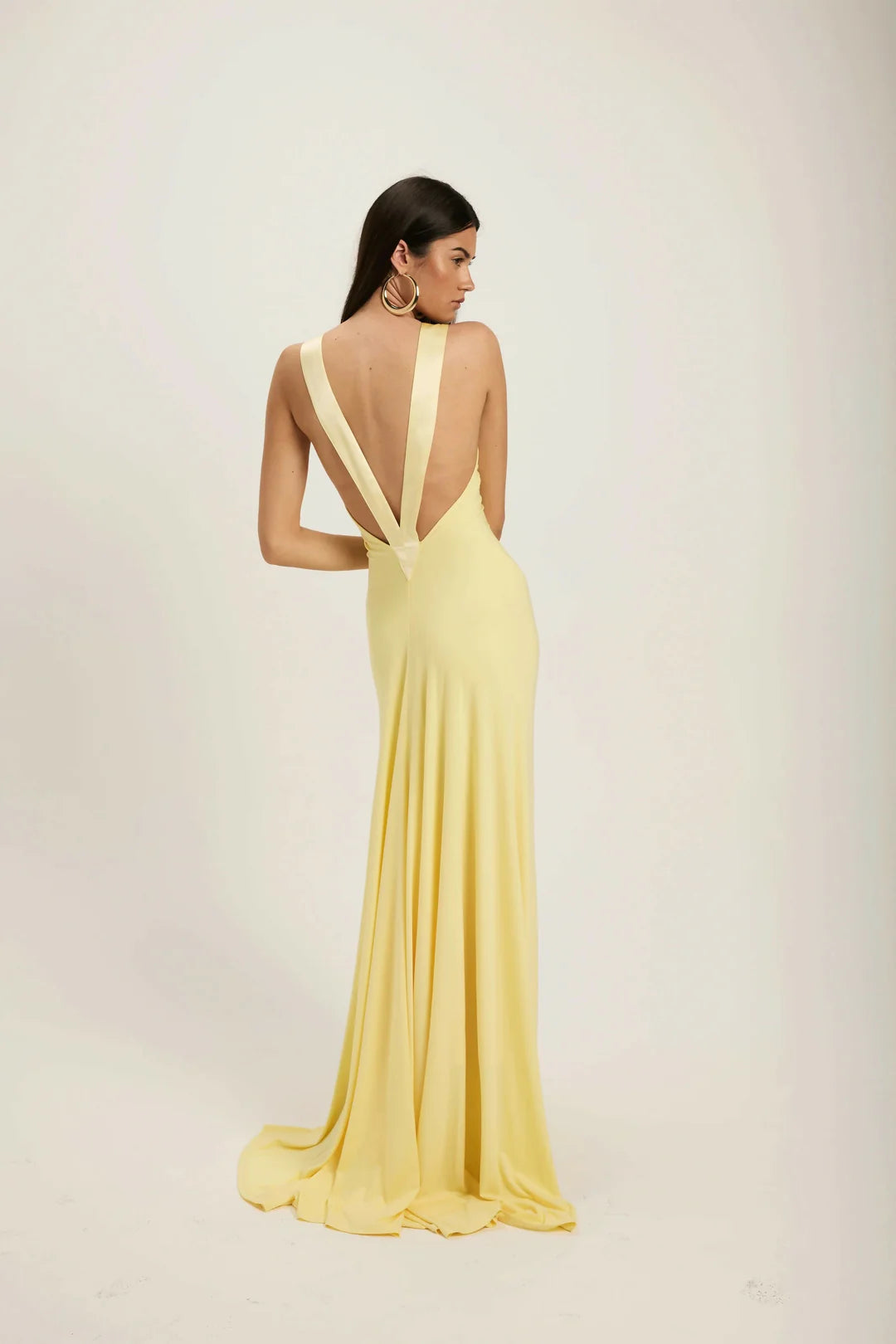 Yellow - A woman modeling a pale yellow, floor-length sleeveless gown featuring a deep plunging V-neckline with a smooth, contrasting trim detail.