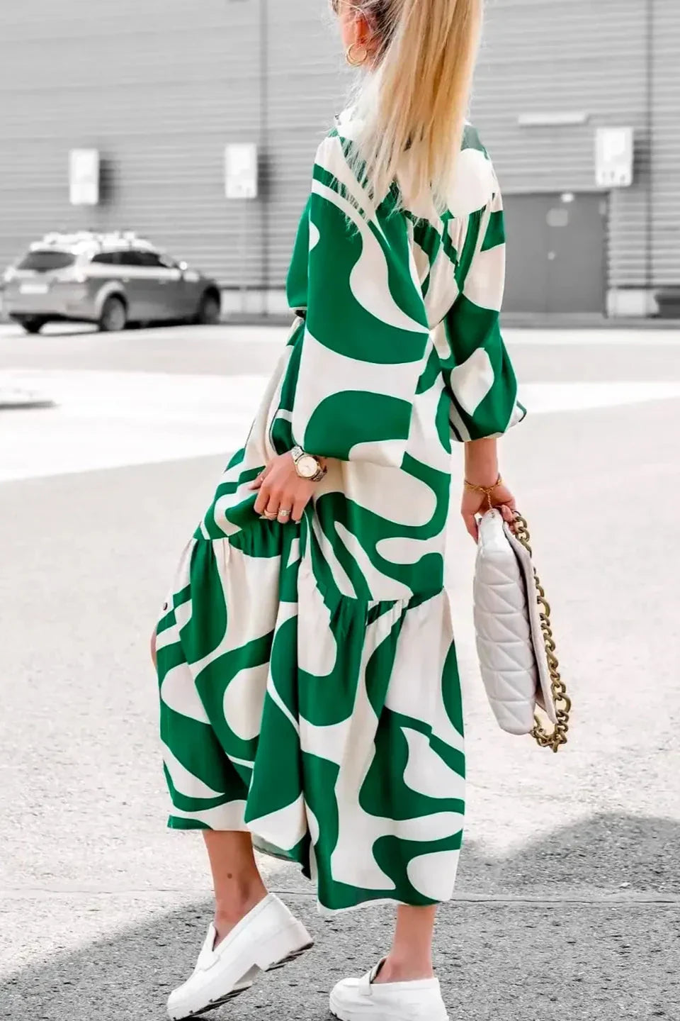 Green - A woman wearing a long, black and white abstract print shirt dress with a tie waist, blouson sleeves, and a high side slit, paired with white chunky loafers.