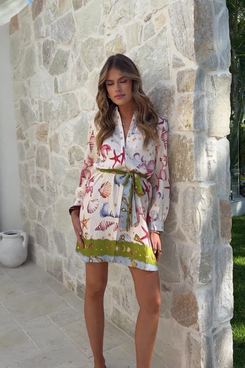 Women's long-sleeve mini shirt dress featuring a vibrant nautical seashell print on a light background, complete with a contrasting patterned tie belt and hem border.