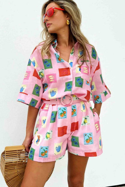 Pink - Women's pink short-sleeve belted playsuit featuring a colourful Mediterranean novelty print with oranges and vases, styled with sunglasses and a bamboo bag.