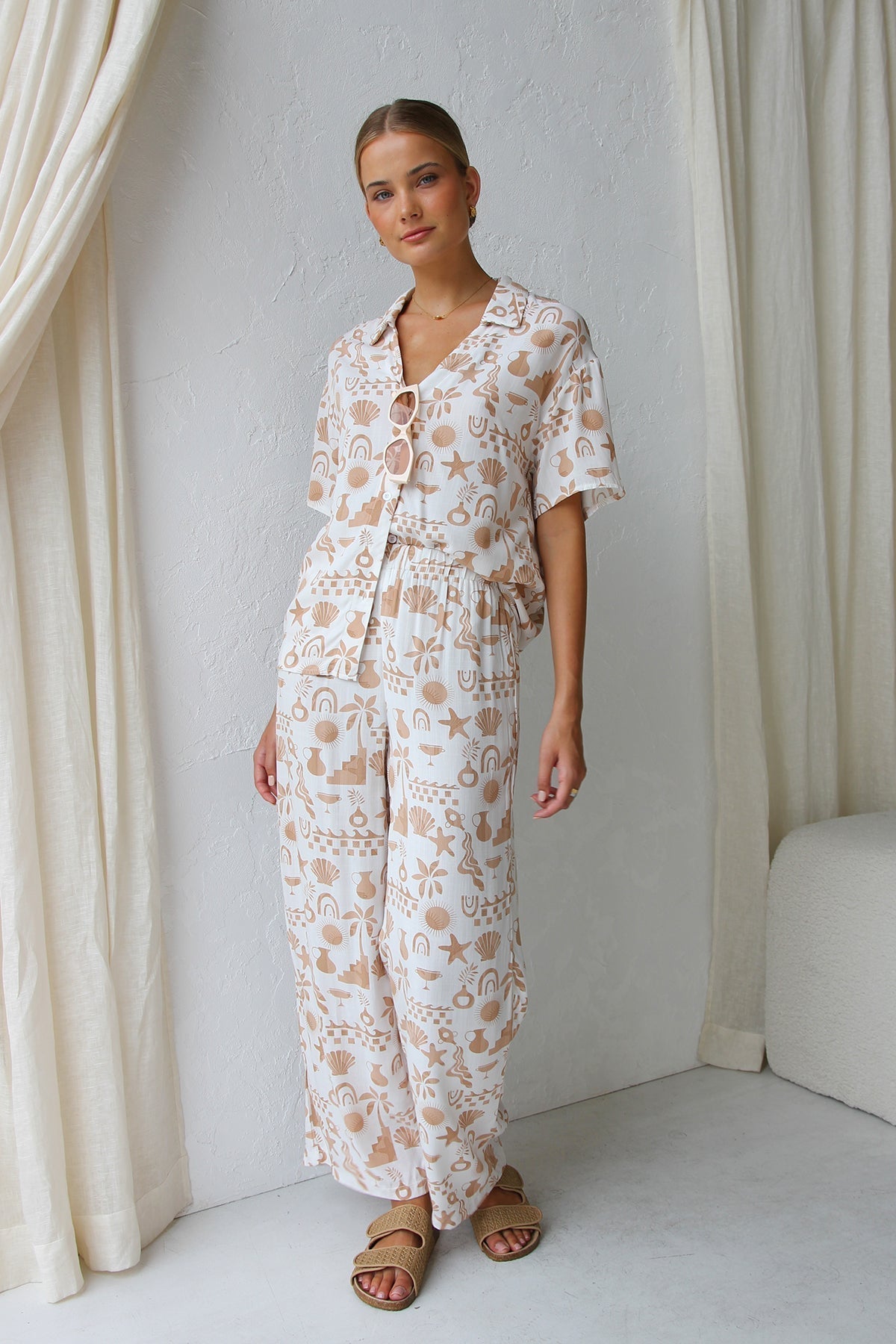 Multicolor - A woman modelling a relaxed-fit, wide-leg trouser and matching short-sleeve shirt co-ord set, featuring a beige coastal vacation print on a white background.