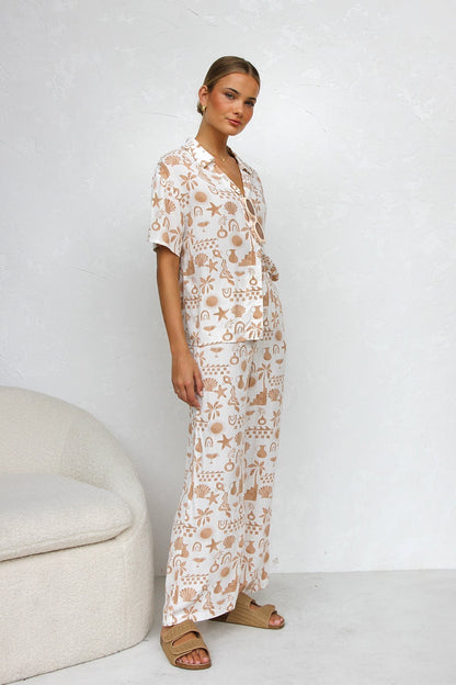 Multicolor - A woman modelling a relaxed-fit, wide-leg trouser and matching short-sleeve shirt co-ord set, featuring a beige coastal vacation print on a white background.