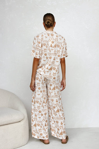 Multicolor - A woman modelling a relaxed-fit, wide-leg trouser and matching short-sleeve shirt co-ord set, featuring a beige coastal vacation print on a white background.