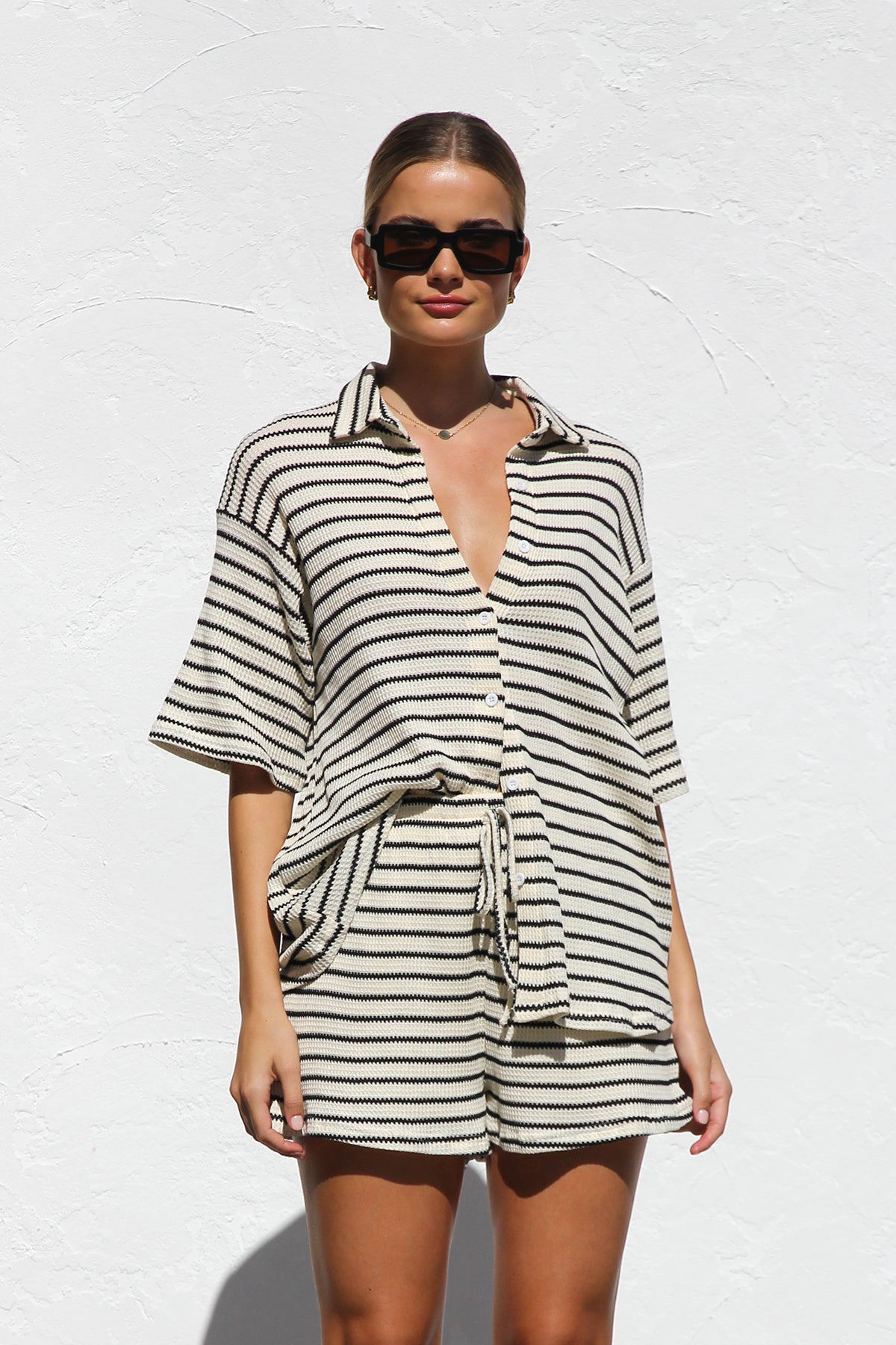 Black - A woman wearing a relaxed-fit, short-sleeve button-down shirt and matching shorts featuring a textured horizontal stripe pattern.