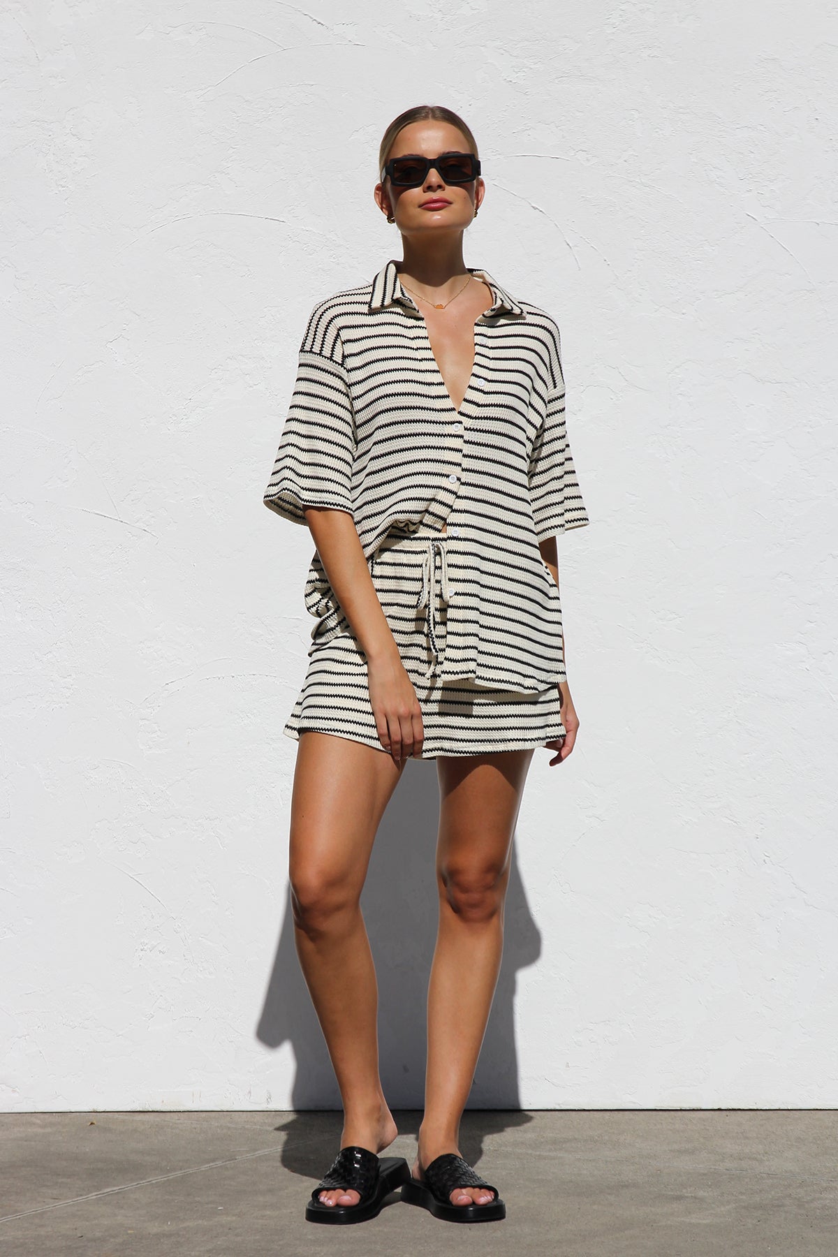 Black - A woman wearing a relaxed-fit, short-sleeve button-down shirt and matching shorts featuring a textured horizontal stripe pattern.