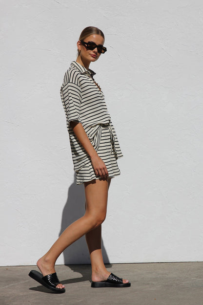 Black - A woman wearing a relaxed-fit, short-sleeve button-down shirt and matching shorts featuring a textured horizontal stripe pattern.