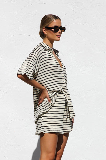 Black - A woman wearing a relaxed-fit, short-sleeve button-down shirt and matching shorts featuring a textured horizontal stripe pattern.