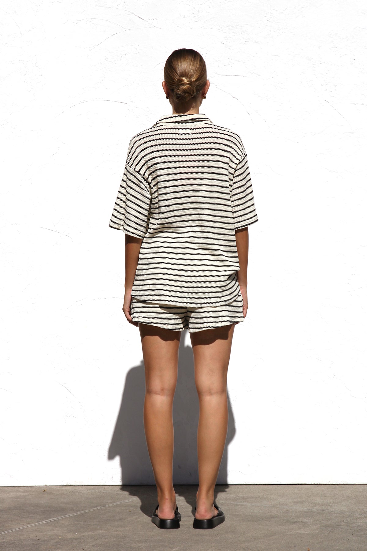 Black - A woman wearing a relaxed-fit, short-sleeve button-down shirt and matching shorts featuring a textured horizontal stripe pattern.
