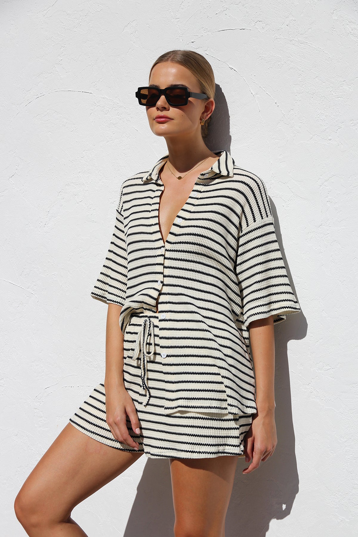 Black - A woman wearing a relaxed-fit, short-sleeve button-down shirt and matching shorts featuring a textured horizontal stripe pattern.