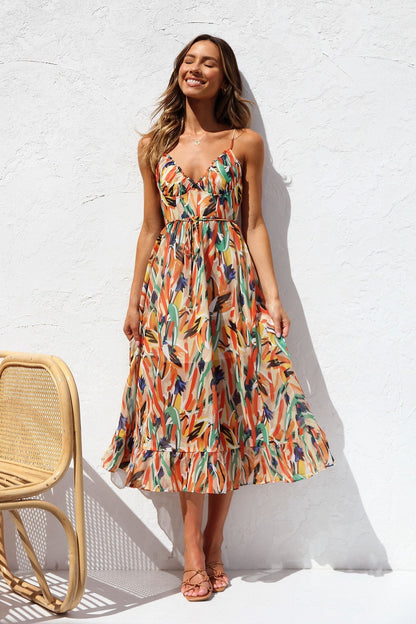 Multicolor - A woman smiling outdoors wearing a vibrant, abstract brushstroke print midi dress featuring a V-neckline, thin straps, a tie waist, and a ruffled hem.