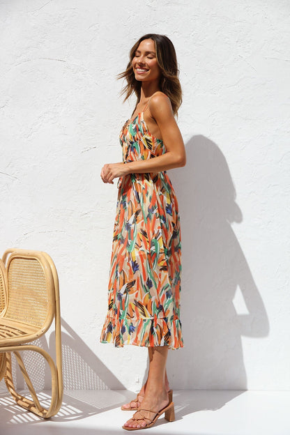 Multicolor - A woman smiling outdoors wearing a vibrant, abstract brushstroke print midi dress featuring a V-neckline, thin straps, a tie waist, and a ruffled hem.