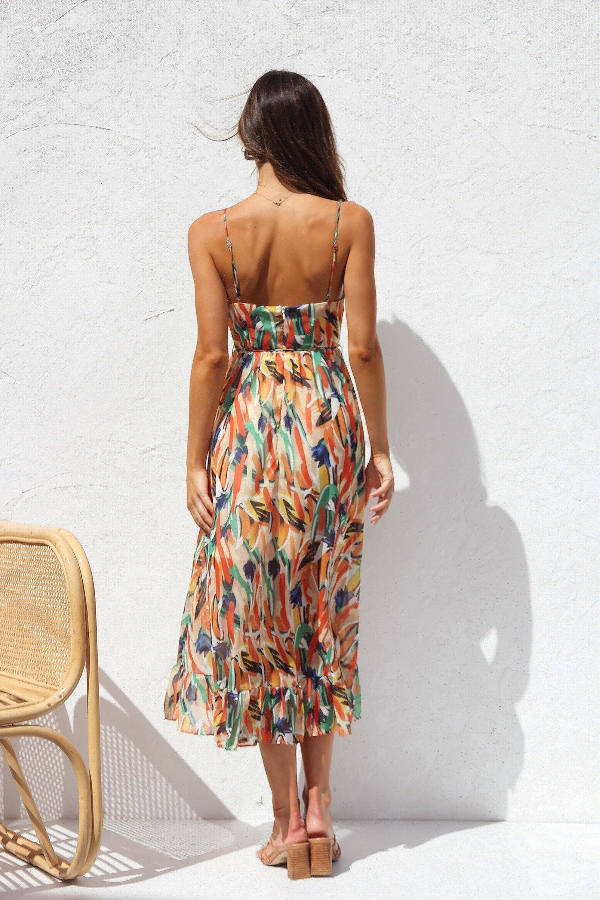 Multicolor - A woman smiling outdoors wearing a vibrant, abstract brushstroke print midi dress featuring a V-neckline, thin straps, a tie waist, and a ruffled hem.