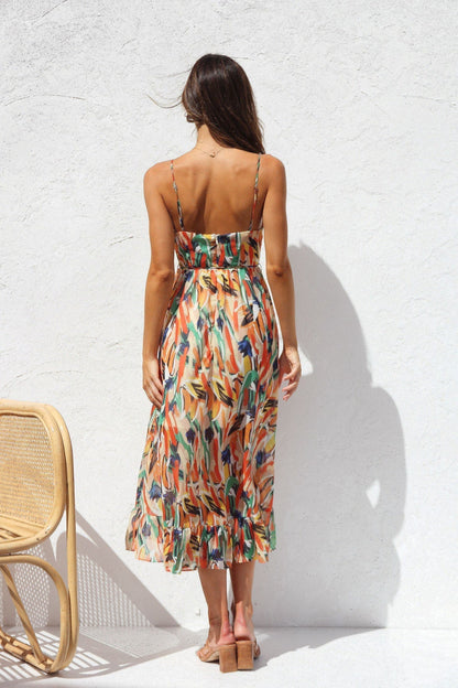 Multicolor - A woman smiling outdoors wearing a vibrant, abstract brushstroke print midi dress featuring a V-neckline, thin straps, a tie waist, and a ruffled hem.