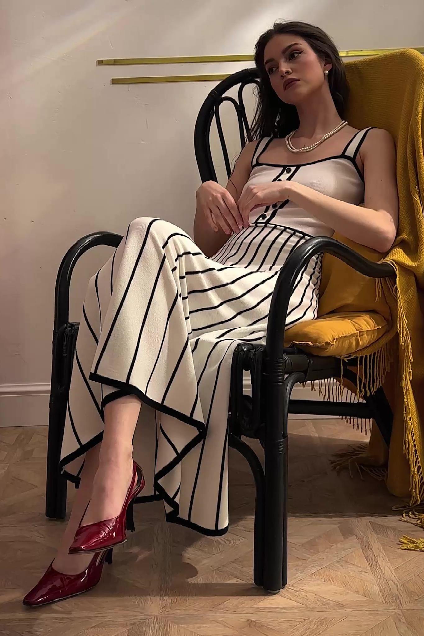 White - Woman wearing an elegant off-white midi knit dress with black contrast binding on the square neckline and straps, a buttoned bodice, and a flared A-line skirt featuring black vertical stripes.