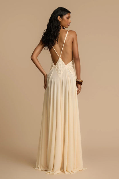 Ivory - A woman wearing an elegant, flowing off-white maxi dress featuring a deep plunging V-neckline and a textured appliqué waist panel, standing against a neutral background.