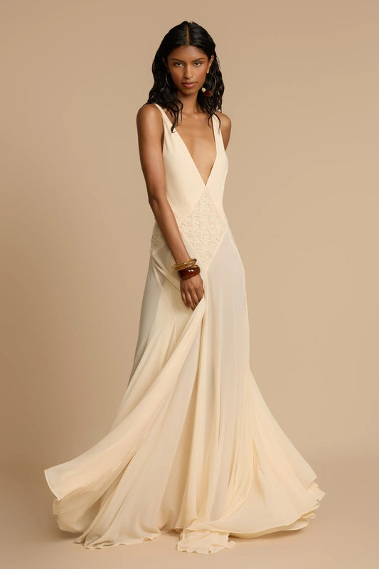 Ivory - A woman wearing an elegant, flowing off-white maxi dress featuring a deep plunging V-neckline and a textured appliqué waist panel, standing against a neutral background.