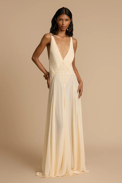 Ivory - A woman wearing an elegant, flowing off-white maxi dress featuring a deep plunging V-neckline and a textured appliqué waist panel, standing against a neutral background.