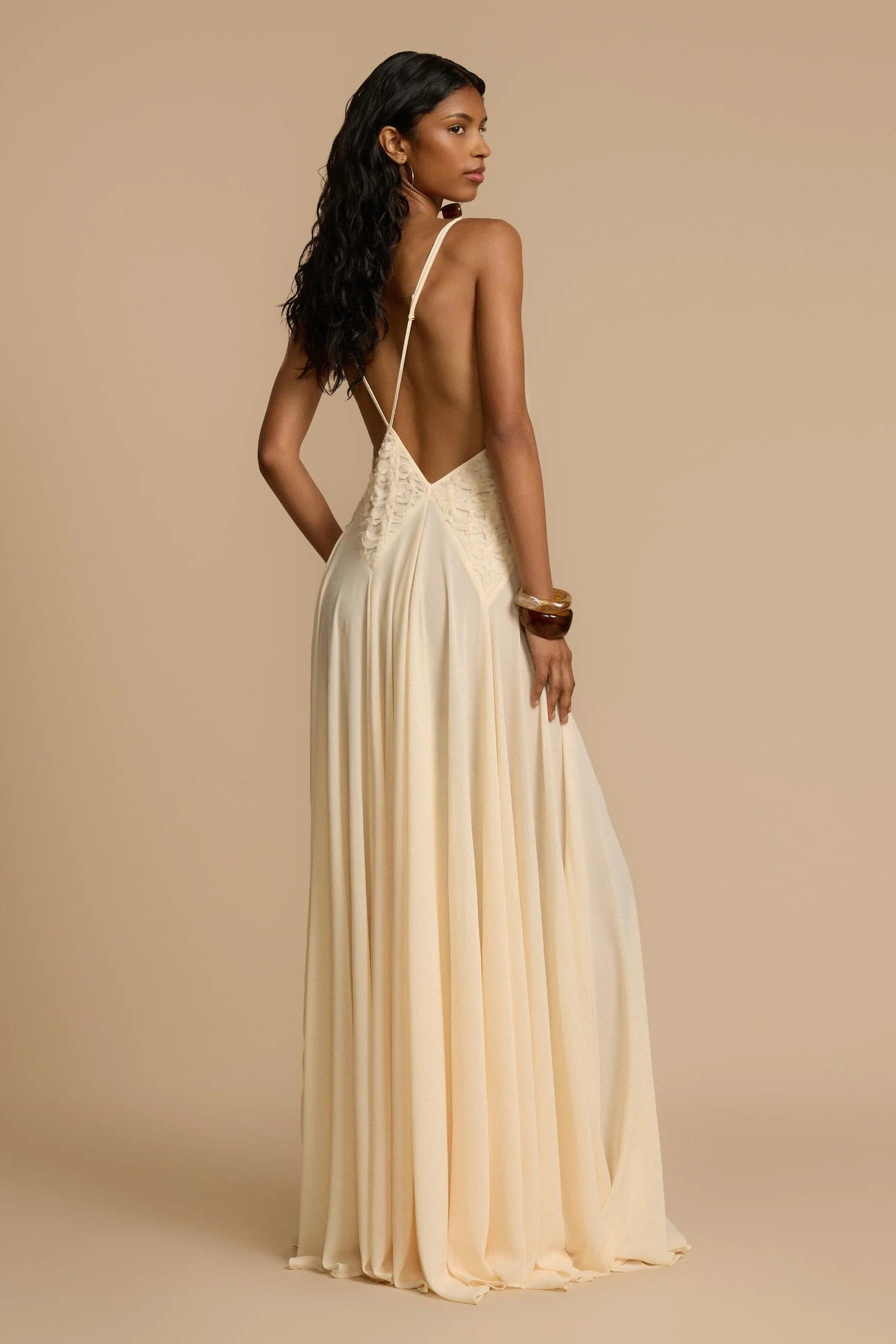 Ivory - A woman wearing an elegant, flowing off-white maxi dress featuring a deep plunging V-neckline and a textured appliqué waist panel, standing against a neutral background.