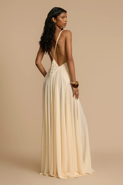 Ivory - A woman wearing an elegant, flowing off-white maxi dress featuring a deep plunging V-neckline and a textured appliqué waist panel, standing against a neutral background.