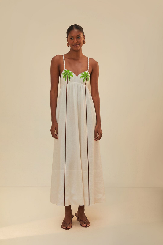 White - A woman wearing a flowing white maxi dress with braided spaghetti straps, a sweetheart neckline featuring embroidered green palm trees on the cups, and long brown vertical stripes down the skirt.