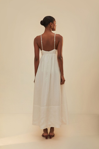 White - A woman wearing a flowing white maxi dress with braided spaghetti straps, a sweetheart neckline featuring embroidered green palm trees on the cups, and long brown vertical stripes down the skirt.