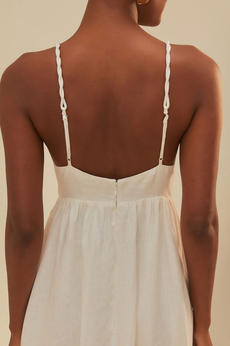 White - A woman wearing a flowing white maxi dress with braided spaghetti straps, a sweetheart neckline featuring embroidered green palm trees on the cups, and long brown vertical stripes down the skirt.
