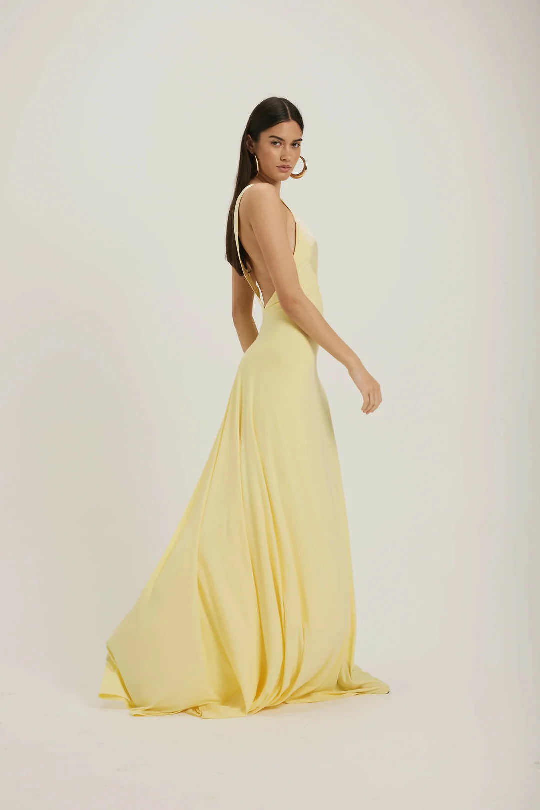 Yellow - A woman modeling a pale yellow, floor-length sleeveless gown featuring a deep plunging V-neckline with a smooth, contrasting trim detail.