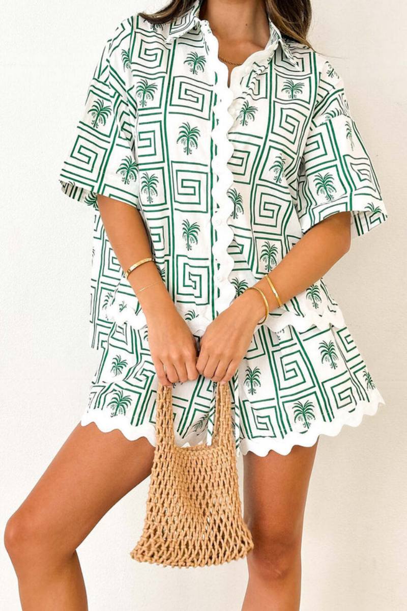 Pink - Model wearing a pink and red geometric palm print matching co-ord set featuring a short-sleeve button-up shirt and shorts with white scalloped trim.