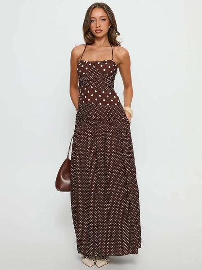 Cocoa - A woman wearing a brown maxi dress featuring a mixed white polka dot print, a halter neckline, a fitted panelled bodice, and a flowing gathered skirt.