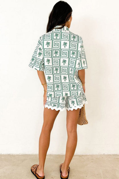 Green - Model wearing a pink and red geometric palm print matching co-ord set featuring a short-sleeve button-up shirt and shorts with white scalloped trim.