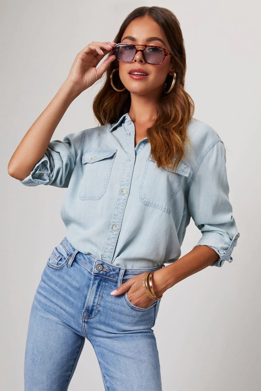 Blue - Women's relaxed-fit chambray button-down shirt featuring dual chest pockets and rolled sleeves, styled with denim jeans.