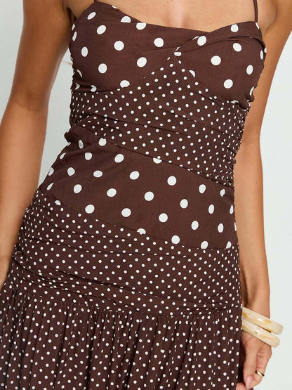 Cocoa - A woman wearing a brown maxi dress featuring a mixed white polka dot print, a halter neckline, a fitted panelled bodice, and a flowing gathered skirt.