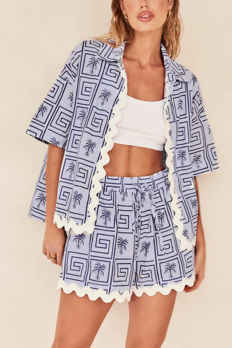 Blue - Model wearing a pink and red geometric palm print matching co-ord set featuring a short-sleeve button-up shirt and shorts with white scalloped trim.