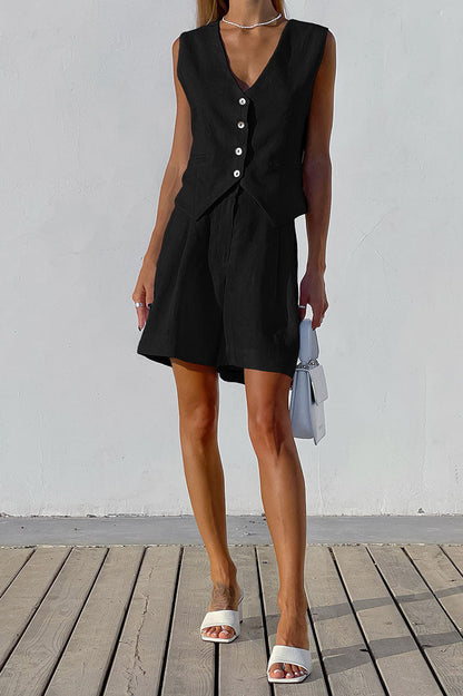 Black - A woman wearing a white, sleeveless, button-front tailored waistcoat top paired with matching high-waisted pleated shorts, standing against a textured white wall.