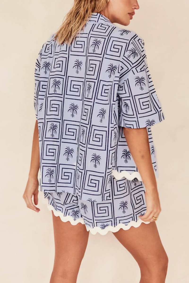 Blue - Model wearing a pink and red geometric palm print matching co-ord set featuring a short-sleeve button-up shirt and shorts with white scalloped trim.