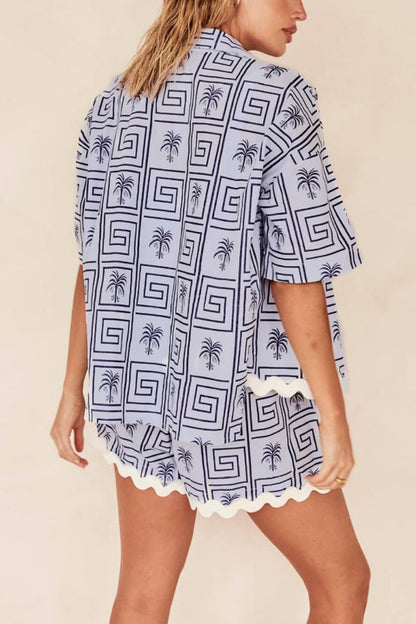 Blue - Model wearing a pink and red geometric palm print matching co-ord set featuring a short-sleeve button-up shirt and shorts with white scalloped trim.