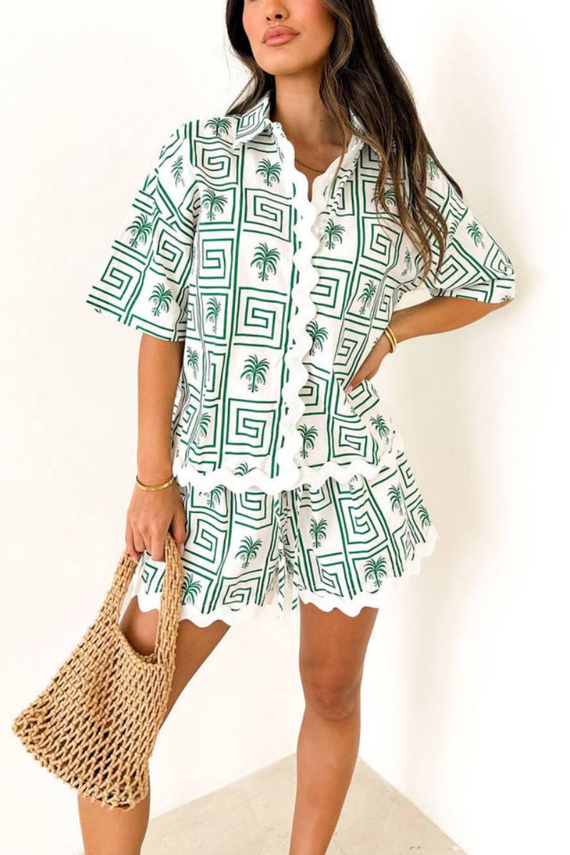 Green - Model wearing a pink and red geometric palm print matching co-ord set featuring a short-sleeve button-up shirt and shorts with white scalloped trim.