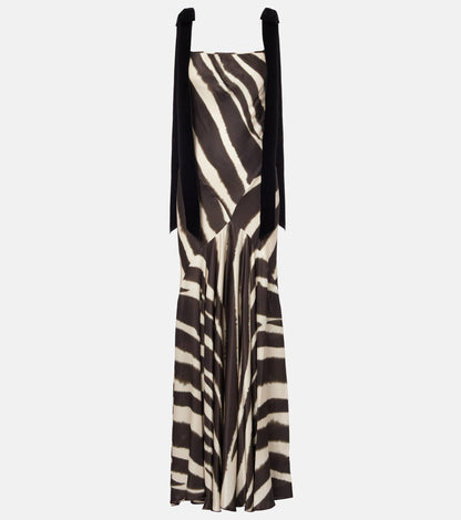 A woman modelling a floor-length, satin-look maxi dress featuring a bold, blurred zebra print and contrasting black textured shoulder ties.